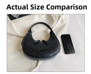Detail of black faux leather crescent bag with crocodile pattern next to a phone