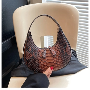 Close-up of a brown crocodile embossed half-moon bag with double zippers on a chair