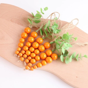 Close-up of Easter wooden carrot bead garlands with green leaves on a light tray