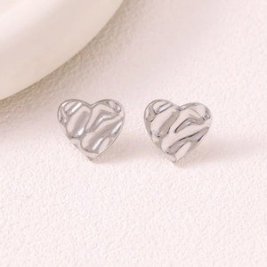 Detailed macro of minimalist silver heart studs with modern hammered water ripple texture