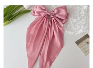 Detail of pink satin bow hair clip with long streamers and silky texture on white lace