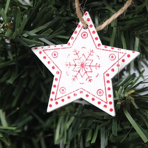 Close-up of white wooden star ornament with red snowflake patterns on green tree branches