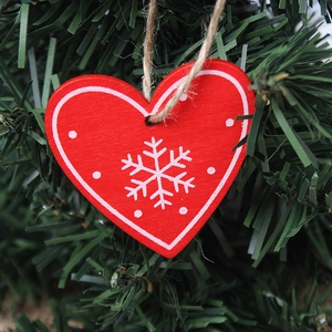 Red heart-shaped wooden Christmas ornament with white snowflakes hanging on a green pine tree