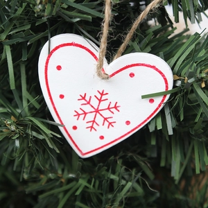 Close-up of wooden heart ornament with red snowflake patterns on green pine branches