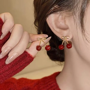 Elegant gold bow and red cherry stud earrings worn with a red knit sweater