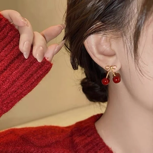 Detail of red cherry earrings with golden bow knot worn on a model in red knitwear