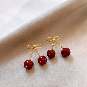 Elegant gold bow and red cherry drop earrings with textured stems on gray background