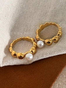 Close-up of golden scalloped bubble rings set with elegant white pearls on fabric