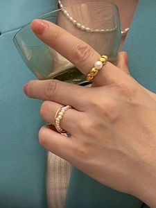 Detail of French vintage gold pearl rings shown on a model holding a green glass