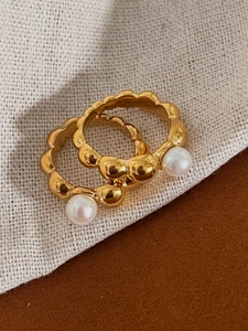 Close-up of golden beaded rings with white freshwater pearls on textured background