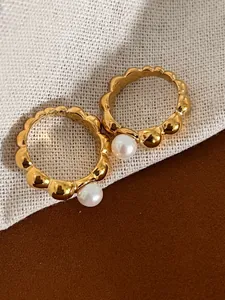 Detail shot of two gold beaded rings featuring white pearls on a minimalist background