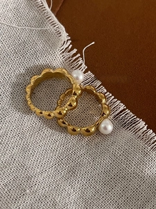 Close-up of gold wavy textured rings with white freshwater pearls on rustic fabric