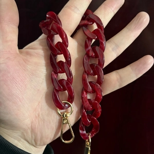 Macro detail of dark red acrylic chain with marble texture and golden metal clasp