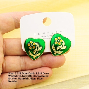 Detail shot of heart-shaped green enamel earrings with gold floral patterns and dimensions