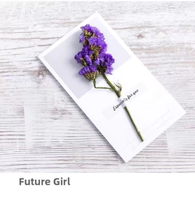 Close-up of a white greeting card with purple dried flowers on a light wood background