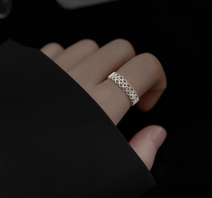 Macro detail of silver lace hollow heart ring showing geometric weave on finger