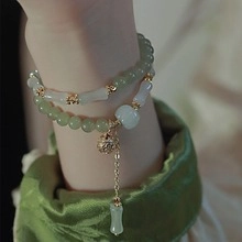 Detail of double-layer beaded bracelet with green jade beads and golden bell charm