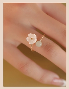 Macro view of gold flower ring featuring white shell petal and green Hetian jade bead