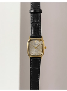 Primo piano di un orologio al quarzo quadrato dorato con cinturino in pelle nera su beige