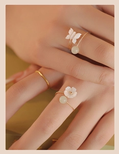 Detail view of gold butterfly and flower rings with green jade beads on model hand