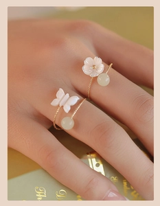 Close-up of gold flower and butterfly open rings with green beads on a female hand