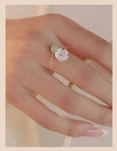 Detail of a gold chain ring featuring a white floral charm and light green jade bead