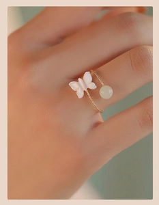 Macro detail of an adjustable gold butterfly ring with a natural white shell and green jade bead