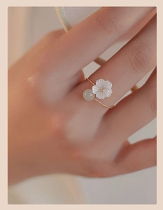 Detailed macro view of a gold floral ring featuring white shell petals and a green jade bead