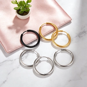 Minimalist stainless steel hoop earrings in gold silver and black set on marble surface