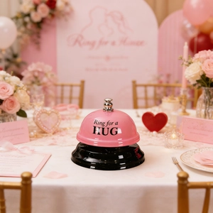 Macro detail of a pink metal service bell with Ring for a HUG text on a romantic table