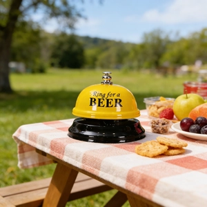 Close-up of yellow metal call bell with Ring for a BEER text on a picnic table