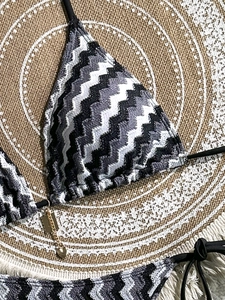 Close-up of zigzag knit bikini with gold heart charm on a summer beach woven mat