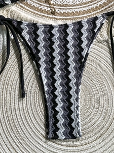 Macro detail of zigzag knit bikini bottoms with black side ties on beach mat