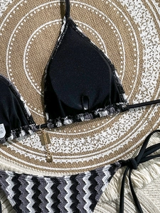 Detail of striped bikini top with zigzag patterns and gold heart-shaped metal pendant