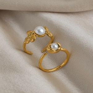 Detail of 18K gold plated flower and pearl stainless steel rings on beige fabric