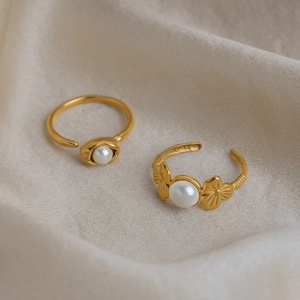 Detail of two adjustable 18K gold plated flower pearl rings on soft white textured fabric