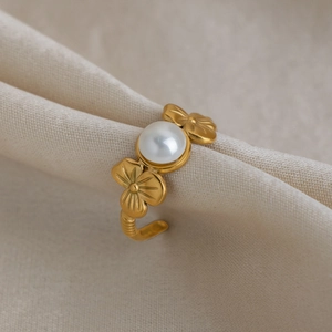 Macro detail of 18K gold-plated floral ring featuring a centered white pearl on silk fabric