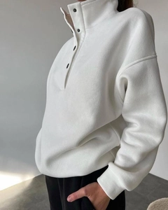 Λεπτομέρεια από λευκό φούτερ fleece με όρθιο γιακά με κουμπιά και χαμηλωμένους ώμους
