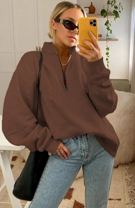 Detail of a brown half-zip sweatshirt with a black zipper and relaxed fit on a model