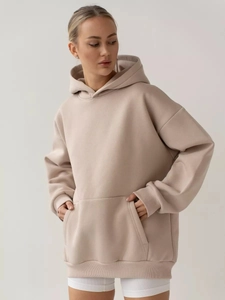 Close-up of the oversized beige hoodie featuring a front kangaroo pocket and ribbed cuffs