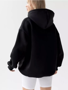 Back view of a black oversized hoodie with ribbed cuffs and dropped shoulders on a model