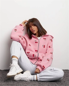 Detail of pink hoodie with cherry print and grey joggers in a cozy sitting pose