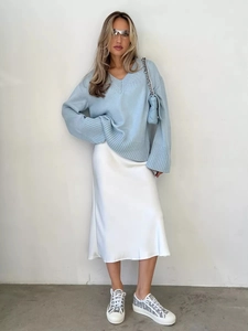 Dettaglio del maglione in maglia celeste con scollo a V e gonna midi in raso bianco