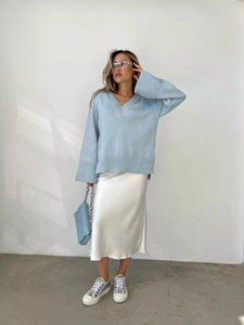 Elegante maglione celeste con scollo a V abbinato a una gonna midi di raso bianco e borsa