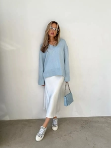 Maglione azzurro con scollo a V abbinato a una gonna in raso bianco e borsa a tracolla