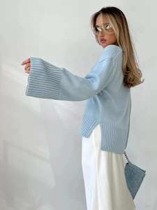 Dettaglio del maglione in maglia azzurro con maniche ampie e spacchi laterali rifiniti