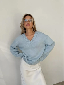 Dettaglio del maglione azzurro con scollo a V oversize e gonna in raso bianco