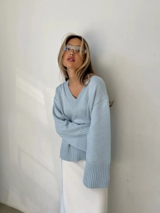Dettaglio dei polsini a costine e scollo a V di un ampio maglione in maglia azzurro