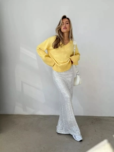 Dettaglio maglione giallo brillante scollo a V e gonna lunga di paillettes argentate