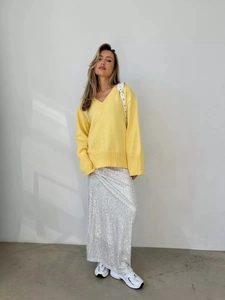 Dettaglio del maglione in maglia giallo chiaro con scollo a V e gonna di paillettes